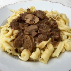 pulled beef stroganoff-679527538 High angle view of beef goulash with mushrooms and noodles served on white plate